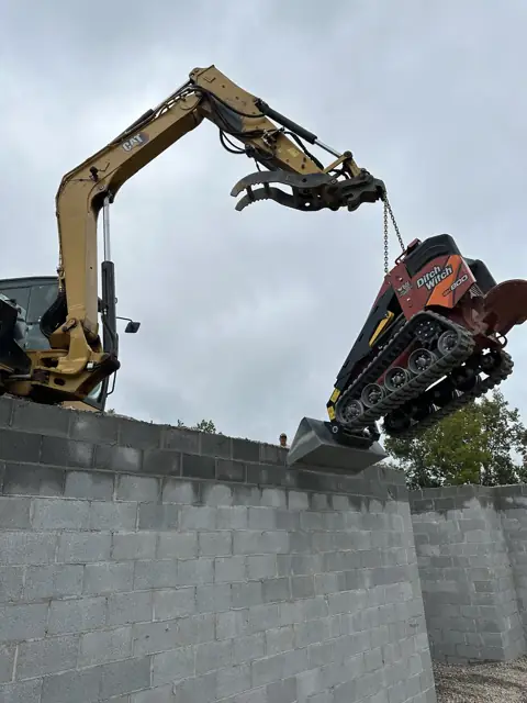 Excavator lifting equipment above a block wall