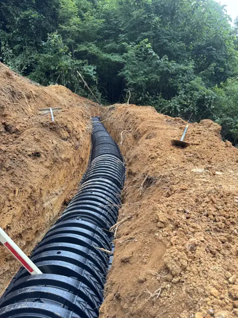 Corrugated lateral line laid in a drain field trench